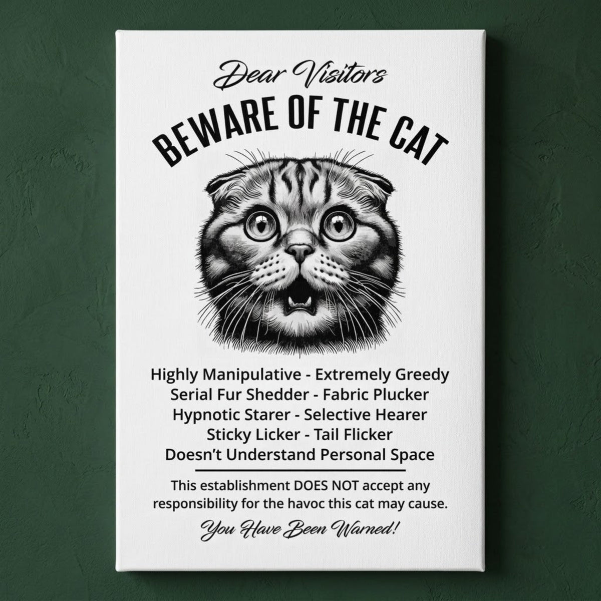 A rectangular white canvas sign with black printed funny text warning visitors about a Scottish Fold cat, featuring a black-and-white illustration and humorous behavioral descriptions. The canvas print is photographed against a dark green wall.