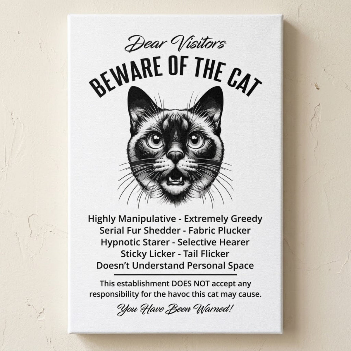A rectangular white canvas sign with black printed funny text warning visitors about a Siamese cat, featuring a black-and-white illustration and humorous behavioral descriptions. The canvas print is photographed against a cream wall.