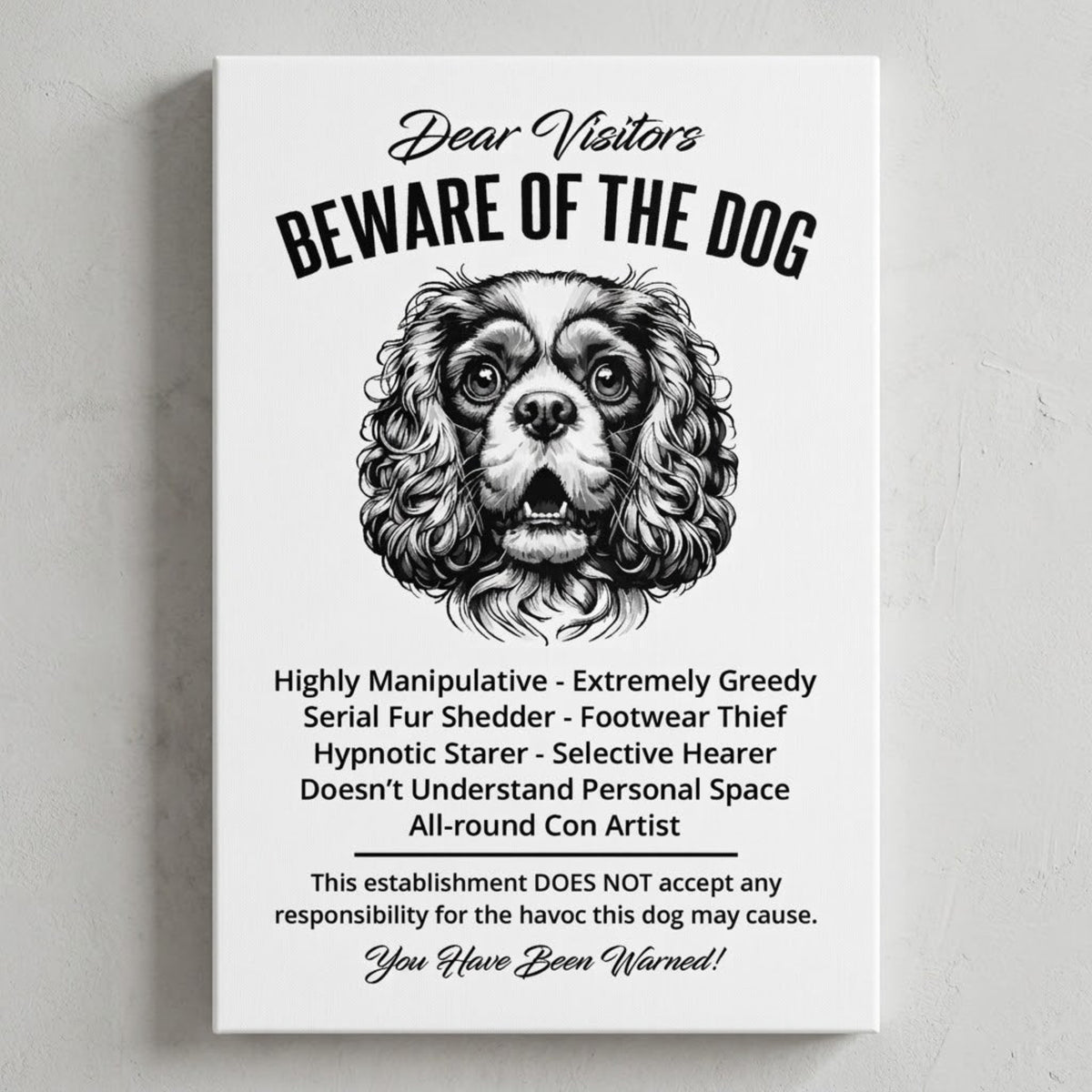 A rectangular white canvas sign with black printed funny text warning visitors about a King Charles Spaniel dog, featuring a black-and-white face illustration and humorous behavioral descriptions. The canvas print is photographed against a light gray wall.