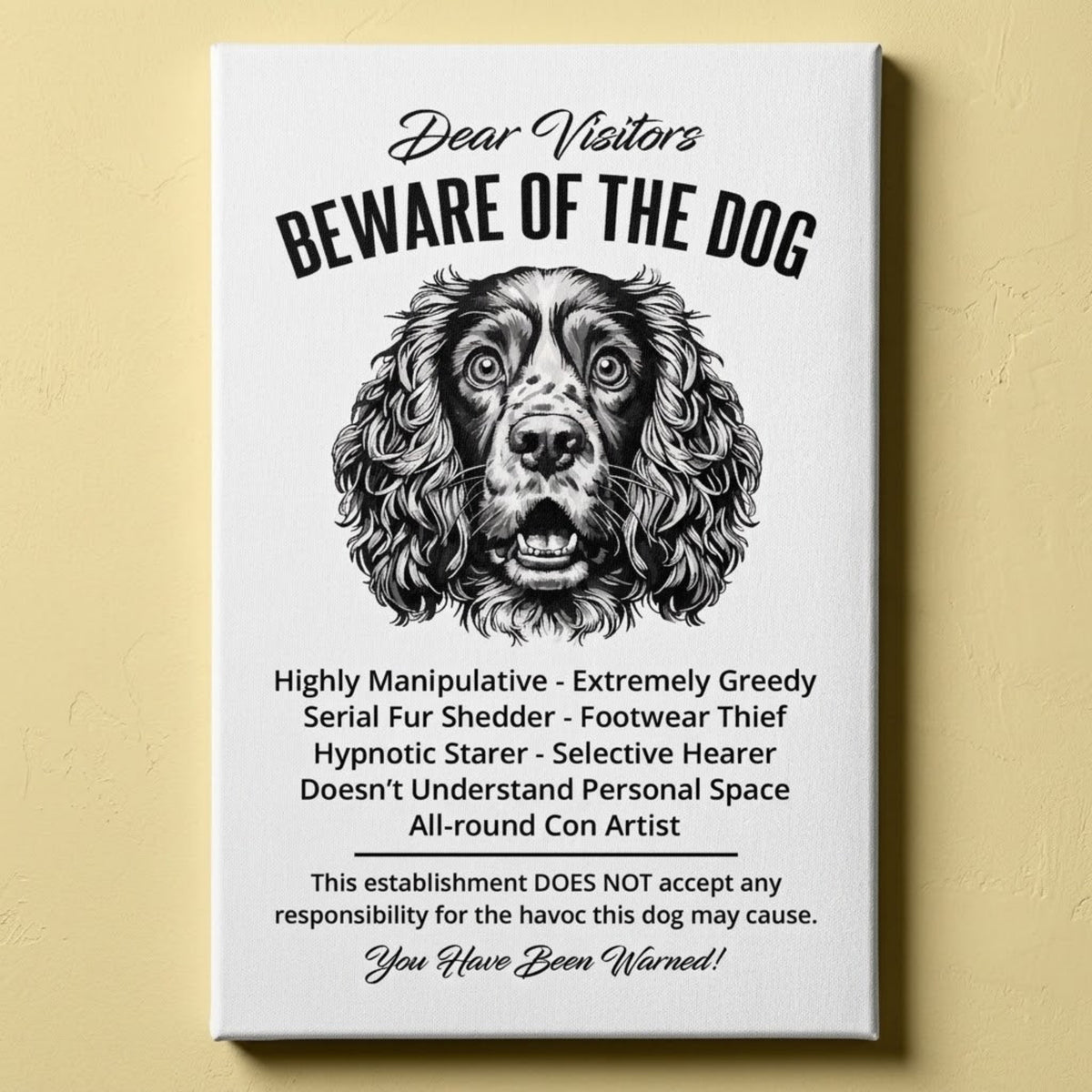 A rectangular white canvas sign with black printed funny text warning visitors about a Springer Spaniel dog, featuring a black-and-white face illustration and humorous behavioral descriptions. The canvas print is photographed against a light yellow wall.