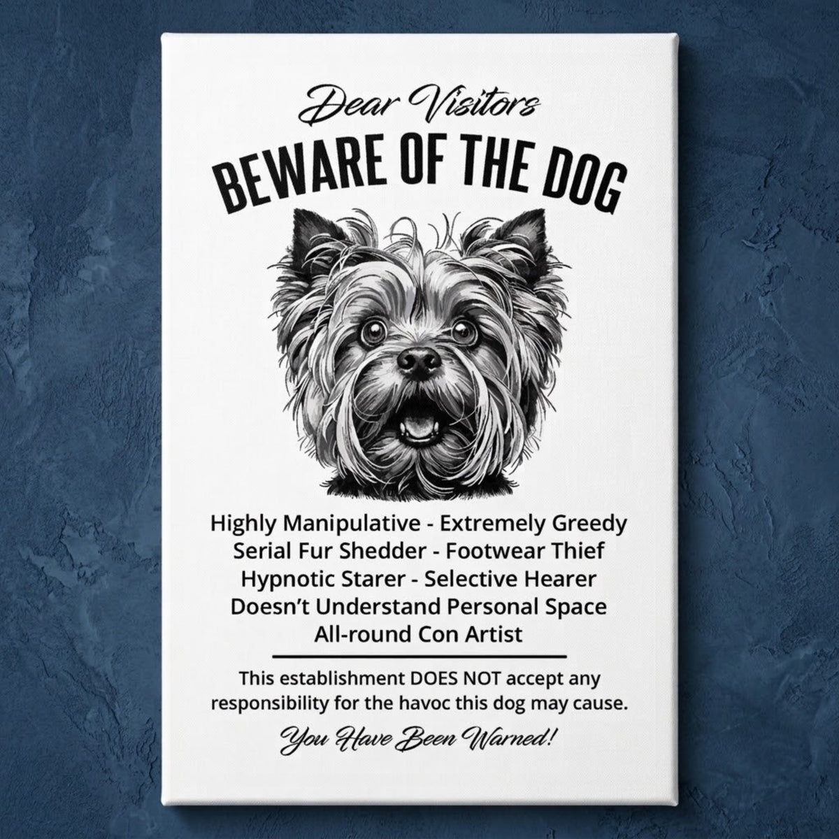 A rectangular white canvas sign with black printed funny text warning visitors about a Yorkshire Terrier dog, featuring a black-and-white face illustration and humorous behavioral descriptions. The canvas print is photographed against a navy blue wall.