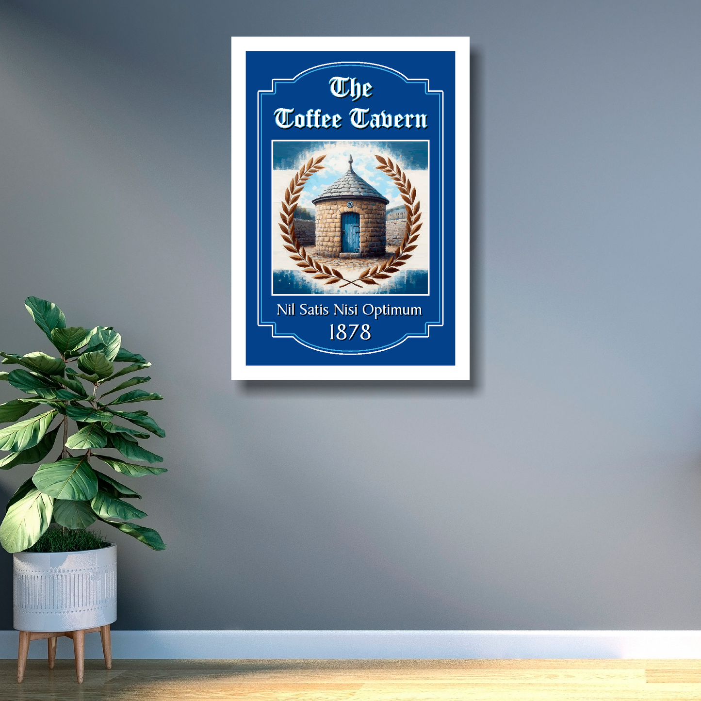 Everton FC white framed artwork of 'The Toffee Tavern' with illustration on a gray wall with a plant below.